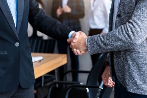 Asian and Caucasian Businessmen Shaking Hands After Successful Negotiations Standing In Modern Office. Two Entrepreneurs Handshaking. Deal, Agreement, Business Partnership Concept. Panorama, Cropped