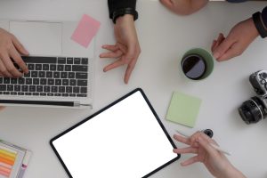Top view of designer team working together in minimal meeting room with mock-up tablet, laptop, camera and designer supplies on white table